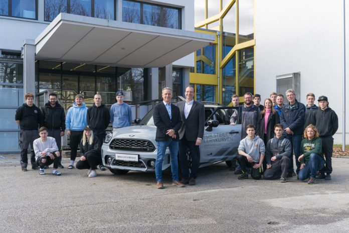 Vor dem MINI: Helmut Buchbauer (Standortleiter AutoFrey Villach, links) und Wolfgang Dumböck (Gebietsleiter BMW Austria, rechts). Neben der Fahrertür (von lilnks) BEd Alexander Steiner, Laureen Buchacher (Assistentin der Standortleitung AutoFrey Villach), Dipl.-Päd. Ing. Joachim Maierwieser (provisorischer Leiter der Schule), BEd Matthias Maurer und BEd Daniel Haid (kniend vorne rechts) mit Schülerinnen und Schülern der Fachberufsschule Villach 2. Foto: AutoFrey/Hannes Pacheiner